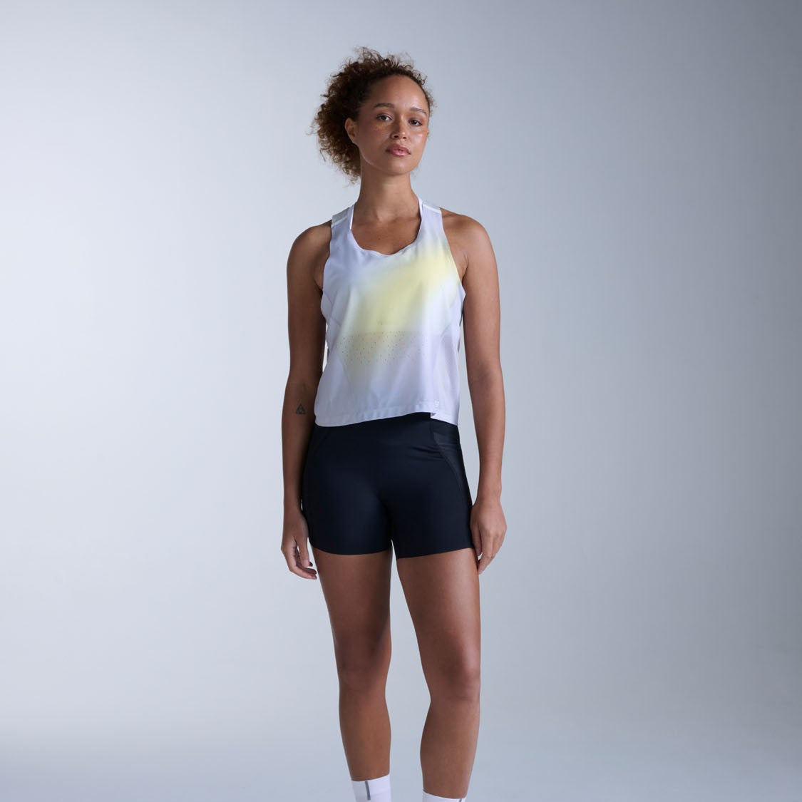 Woman wearing a white tank top with yellow gradient and black shorts on a light gray background
